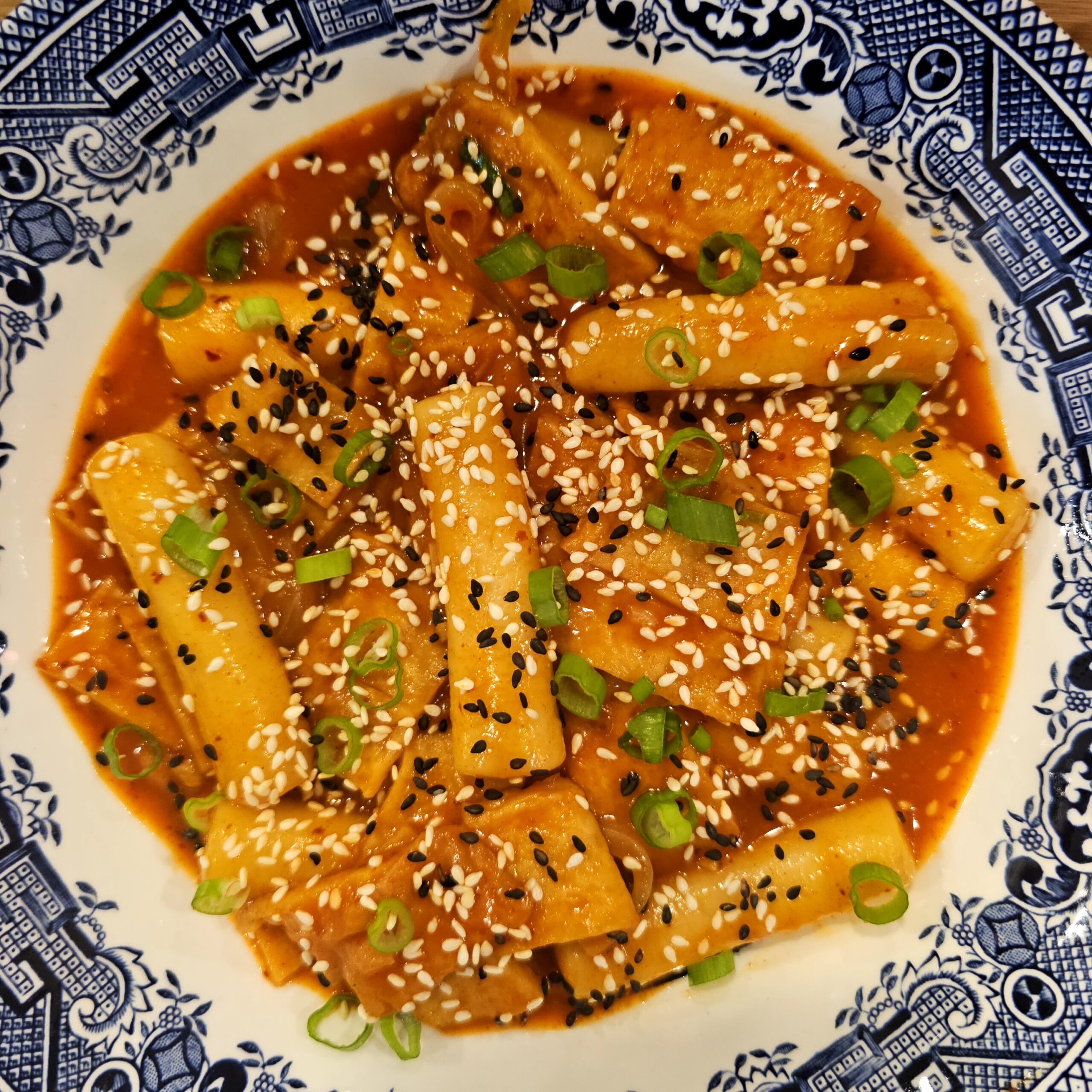 Close up shot of tteokbokki showing the glossy spicy sauce and fresh green onion garnish.