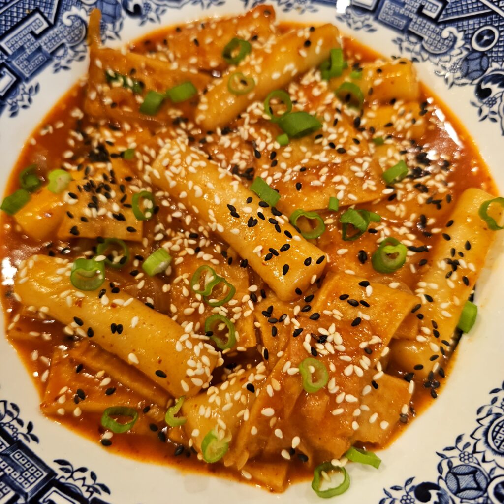Close up shot of tteokbokki showing the glossy spicy sauce and fresh green onion garnish.