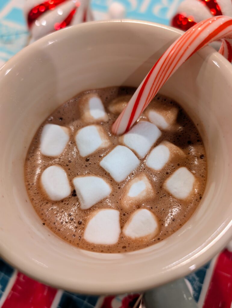 Extreme close-up of rich hot chocolate topped with melting mini marshmallows and a peppermint candy cane.