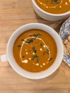 Overhead view of creamy tomato soup in a white bowl garnished with cream and herbs.