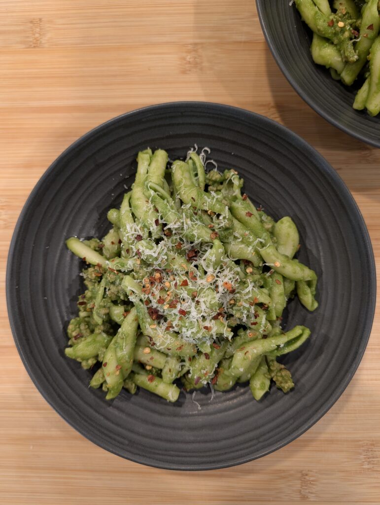 Looking down at a bowl of green goddess pasta with visible pieces of Italian sausage and parmesan garnish.