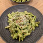 A bowl of green goddess pasta with sausage garnished with cheese and crushed red pepper.
