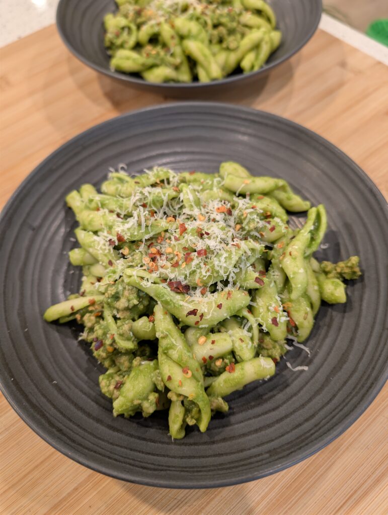 A bowl of green goddess pasta with sausage garnished with cheese and crushed red pepper.