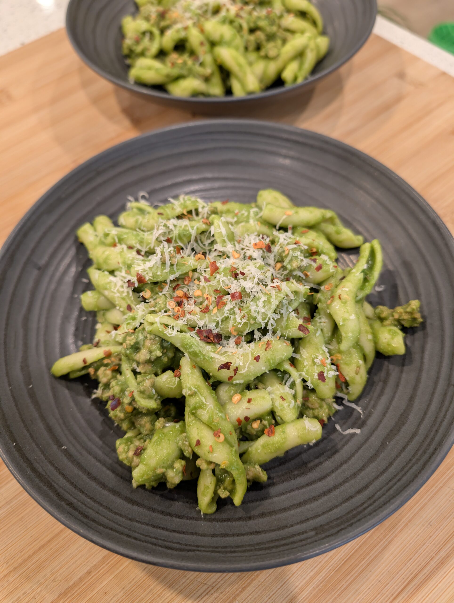 A bowl of green goddess pasta with sausage garnished with cheese and crushed red pepper.
