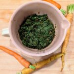 Overhead view of carrot top chimichurri in a pink ceramic bowl with rainbow carrots on a wooden cutting board
