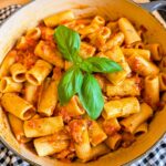 Overhead view of rigatoni pasta coated in rich tomato sauce and garnished with fresh basil in a cooking pot.
