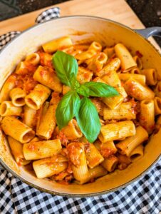 Overhead view of rigatoni pasta coated in rich tomato sauce and garnished with fresh basil in a cooking pot.