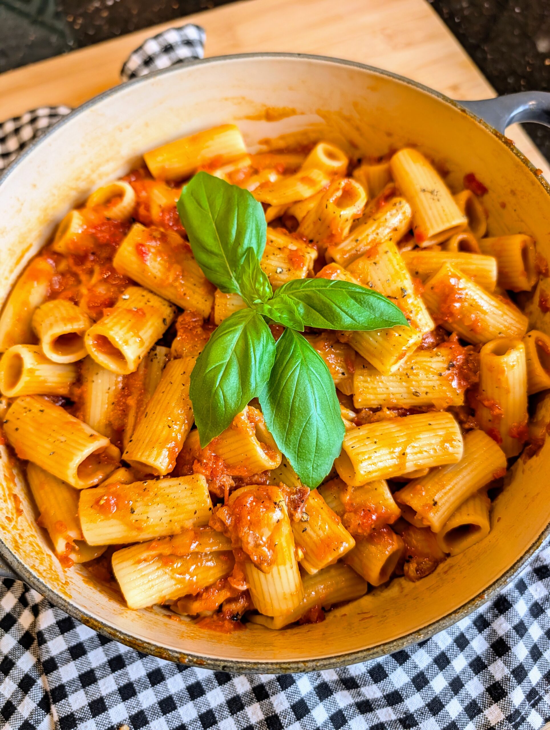Overhead view of rigatoni pasta coated in rich tomato sauce and garnished with fresh basil in a cooking pot.