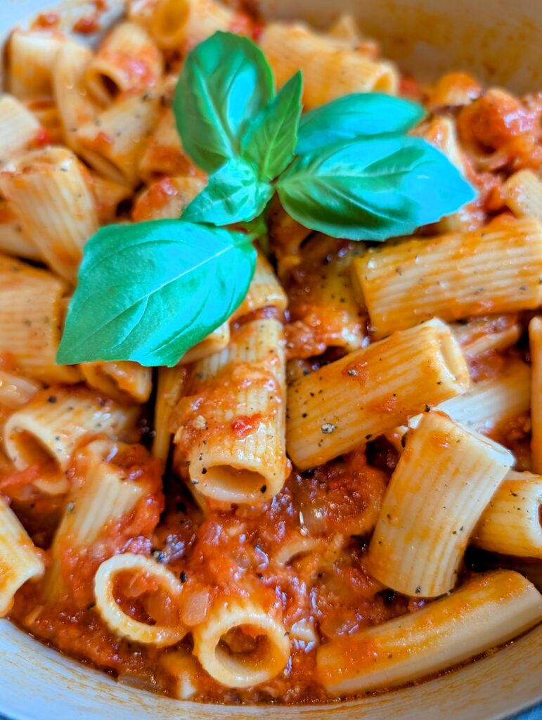 Extreme close up shot of rigatoni pasta coated in thick tomato sauce and crushed black pepper with fresh basil.