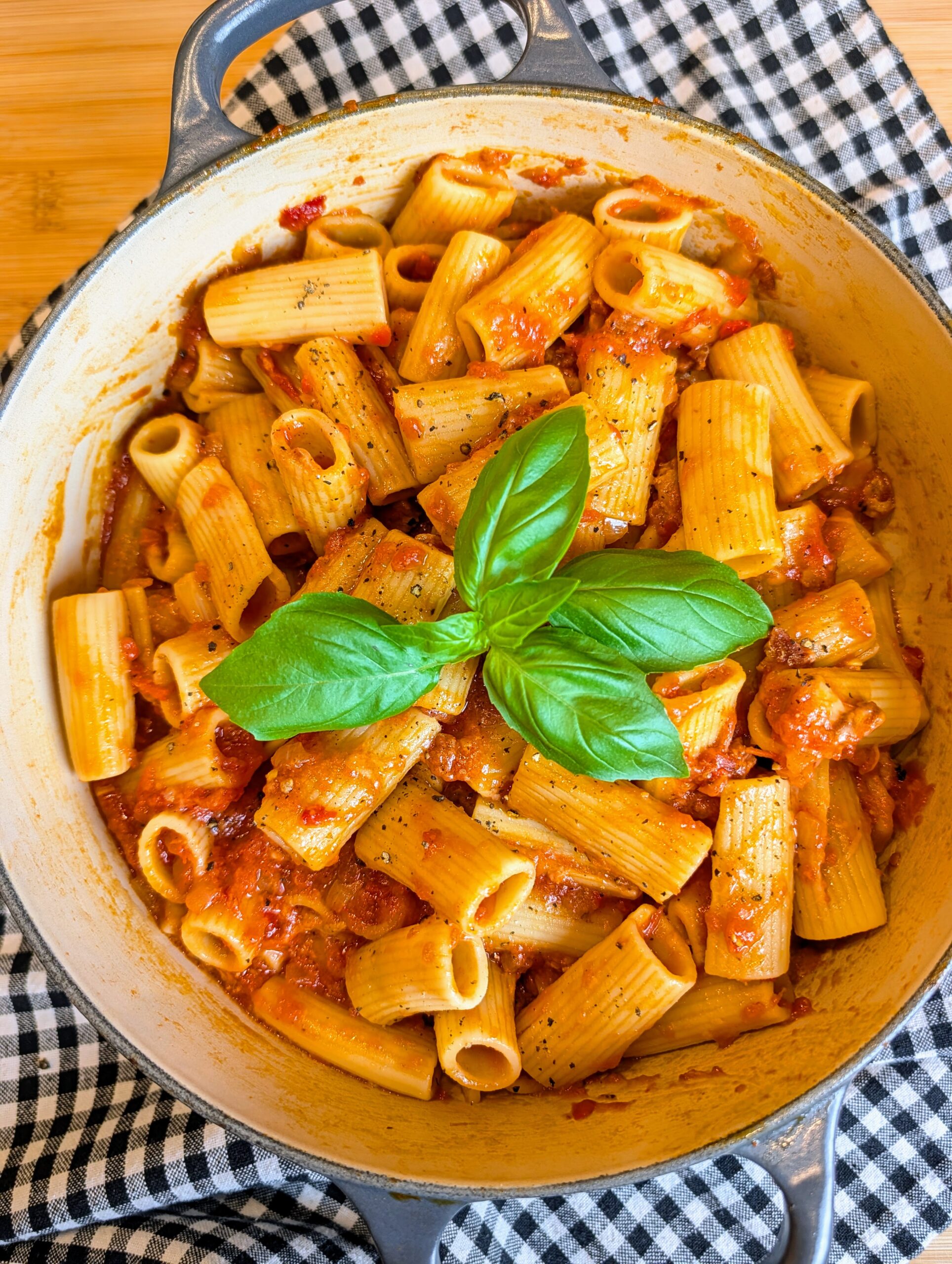 Overhead view of rigatoni pasta coated in rich tomato sauce and garnished with fresh basil in a cooking pot.